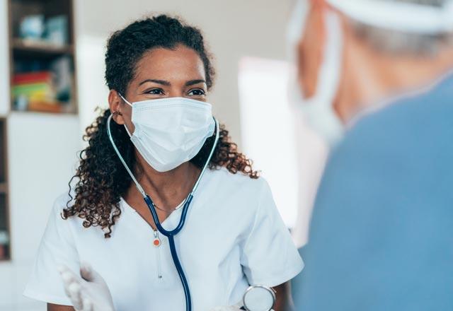 A nurse wearing a mask speaks to a patient.
