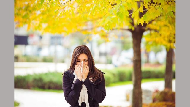 woman blowing nose in front of yellow trees